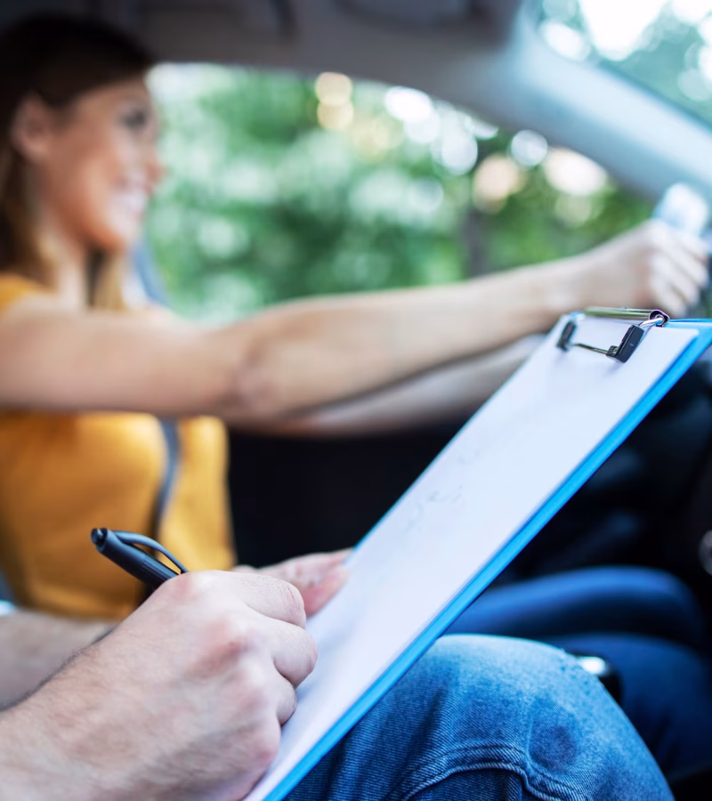 vista-ravvicinata-dell-istruttore-di-guida-tenendo-la-lista-di-controllo-mentre-in-background-studentessa-sterzo-e-guida-di-auto_342744-688 (1)